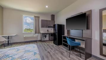 Una habitación de hotel moderna con una cama grande, un escritorio, una kitchenette y un televisor montado en la pared.
