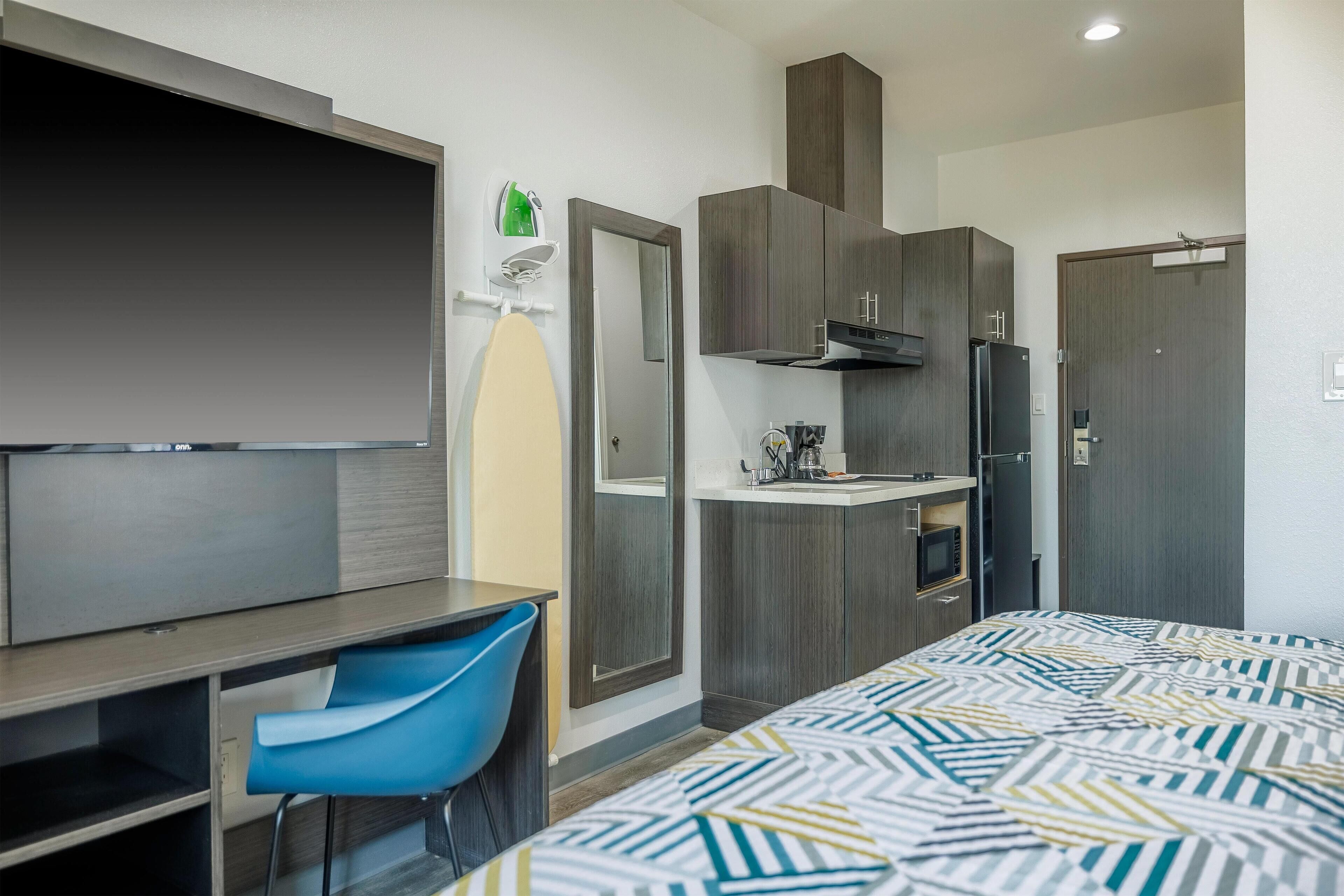 Habitación de hotel con cama, escritorio, silla, televisor, kitchenette y armario.