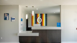 A reception area with a modern design, featuring a counter, a large number '6' on the wall, and several informational posters. - Studio 6 – Giddings, Tx (Giddings)