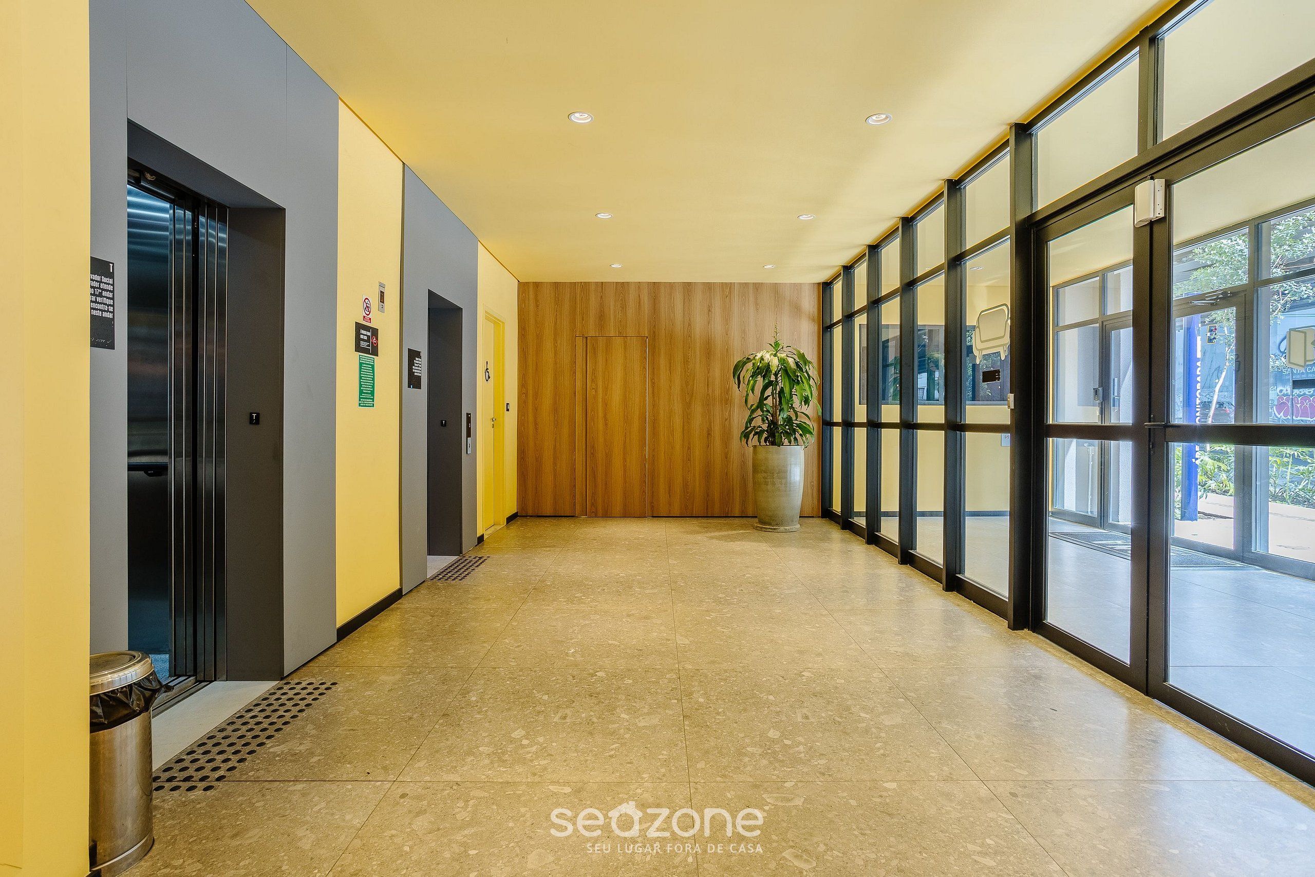 Un pasillo moderno con un panel de madera, un cubo de basura y una planta en maceta.