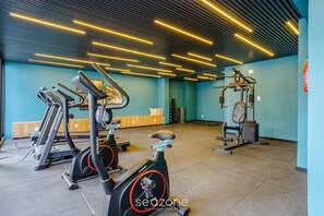 Un gimnasio con equipo de ejercicio, una pared azul y un techo con luces lineales.