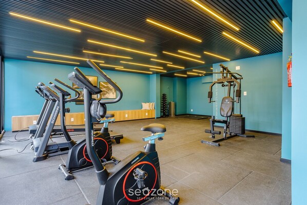 A gym with exercise equipment, a blue wall, and a ceiling with linear lights.