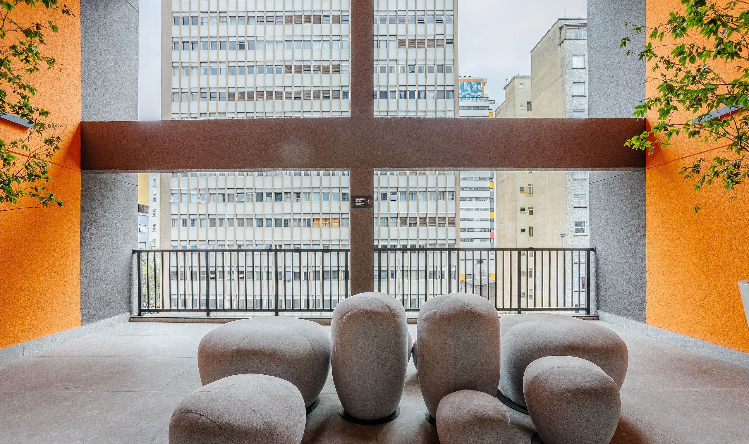 Varanda com vista para edifícios altos, com grade de metal e várias áreas de estar acolchoadas.