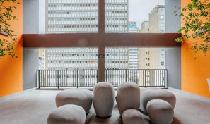 Een balkon met uitzicht op hoge gebouwen, met een metalen hekwerk en meerdere zithoeken met kussens.