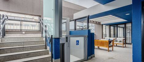 Un bâtiment moderne aux couleurs bleu et gris, doté d’un escalier, d’une porte accessible aux personnes à mobilité réduite et d’un espace détente avec une table et des chaises.
