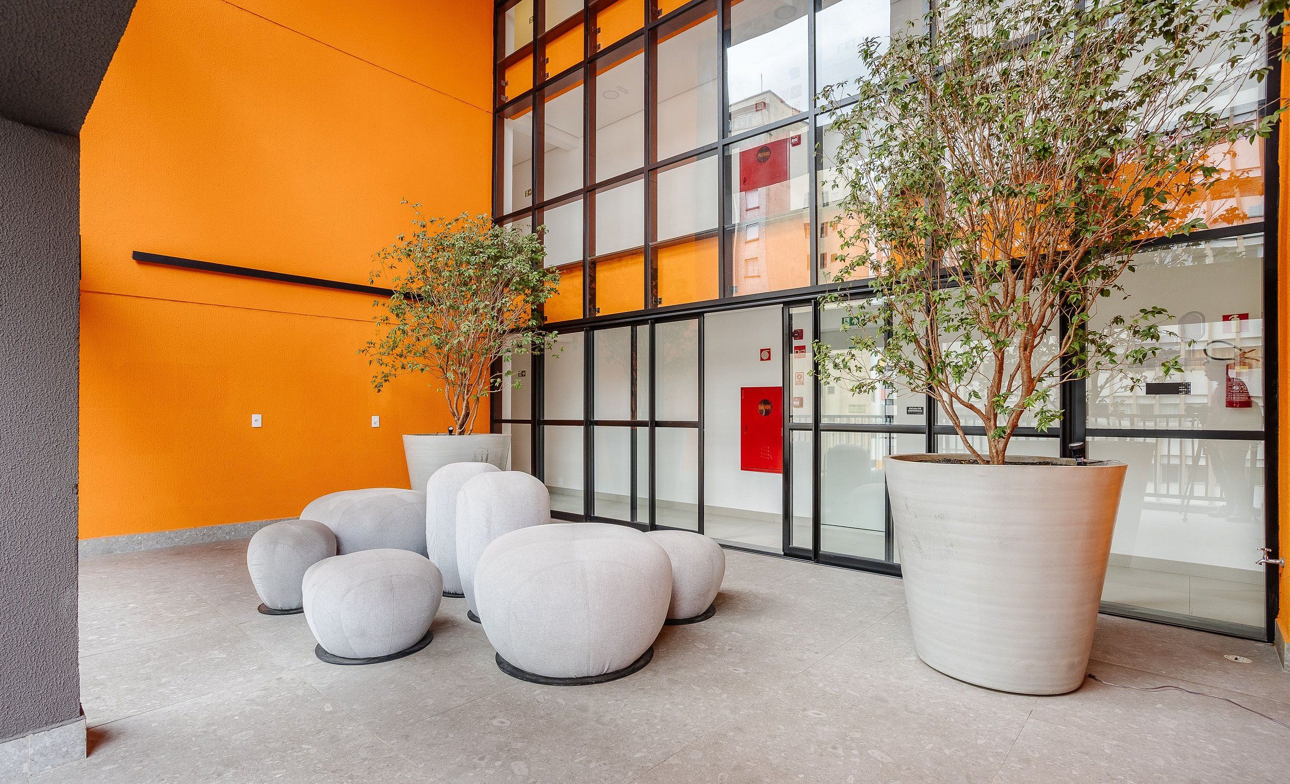 A modern indoor space with large potted plants, seating areas, and a glass wall reflecting the building's interior.