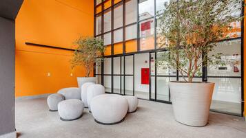 A modern indoor space with large potted plants, seating areas, and a glass wall reflecting the building's interior.