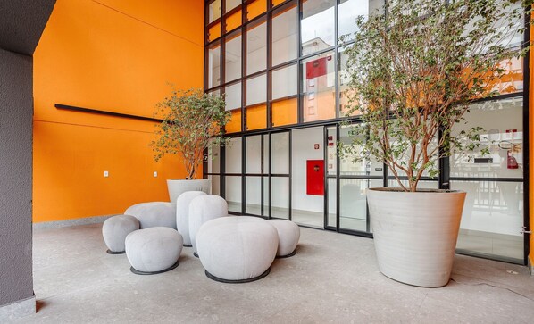 Un espace intérieur moderne, agrémenté de grandes plantes en pot, de coins salon et d’un mur de verre qui reflète l’intérieur du bâtiment.
