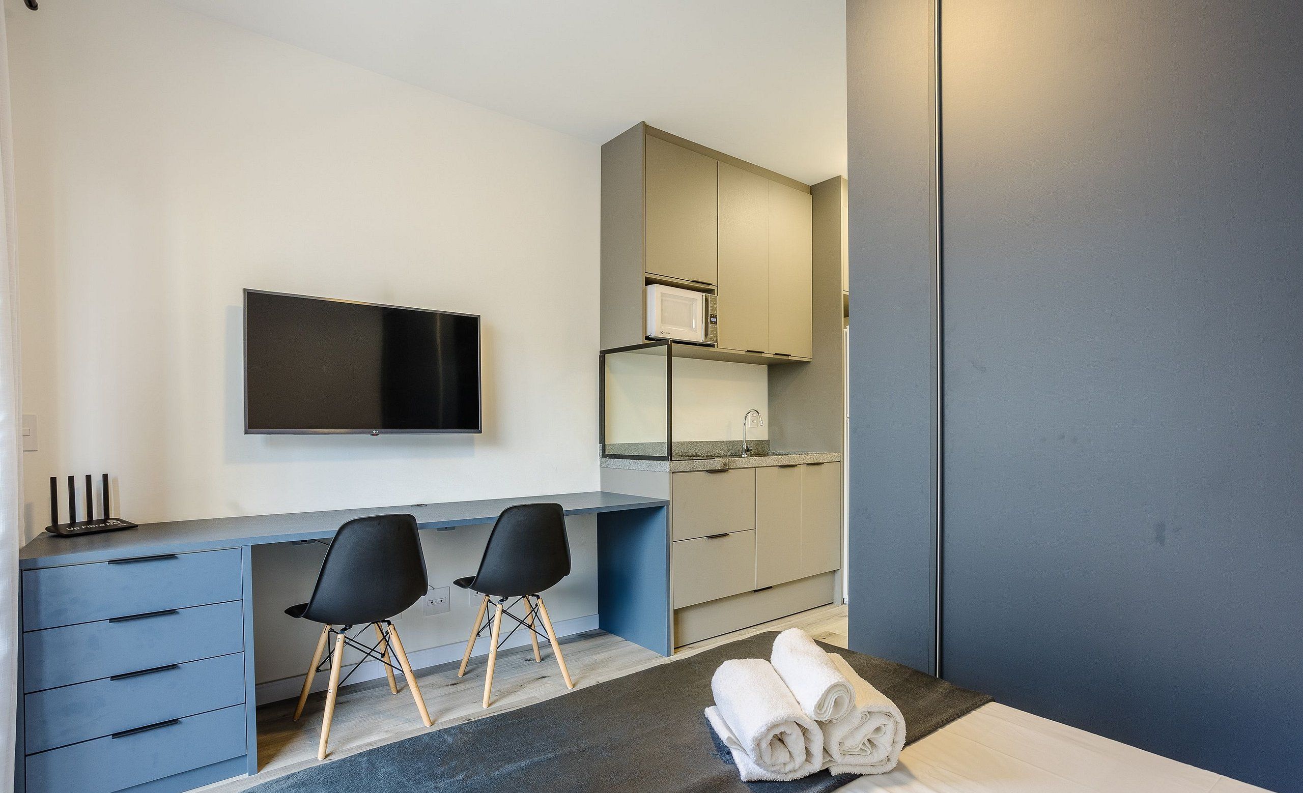 Un dormitorio moderno con cama, escritorio, dos sillas, televisor y kitchenette.