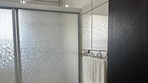 A shower with frosted glass doors, a towel rack with a white towel, and a dark door. - Vista Bela Residential - Apt 07 (Centro Bombinhas)