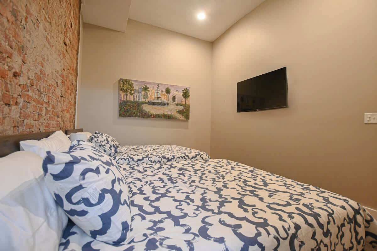 Ein Schlafzimmer mit Backsteinwand, einem Gemälde, einem Flachbildfernseher und einer geblümten Bettdecke.