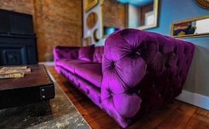 Een paarse bank in een kamer met een bakstenen muur en een blauwe muur met ingelijste foto's.