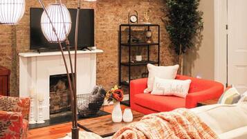 Ein Wohnzimmer mit Backsteinwand, Kamin, einem roten Sofa, einem weißen Sessel und einem Couchtisch mit Blumenvase.