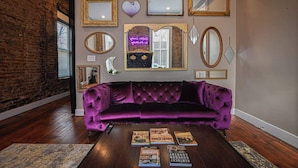 Una habitación con un sofá de terciopelo morado, una mesa de centro con libros y varios espejos enmarcados en la pared.