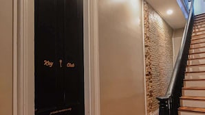Un pasillo con una puerta negra, escaleras de madera y una pared de ladrillo.