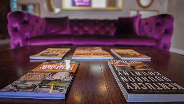 Una mesa con libros y un sofá morado al fondo.