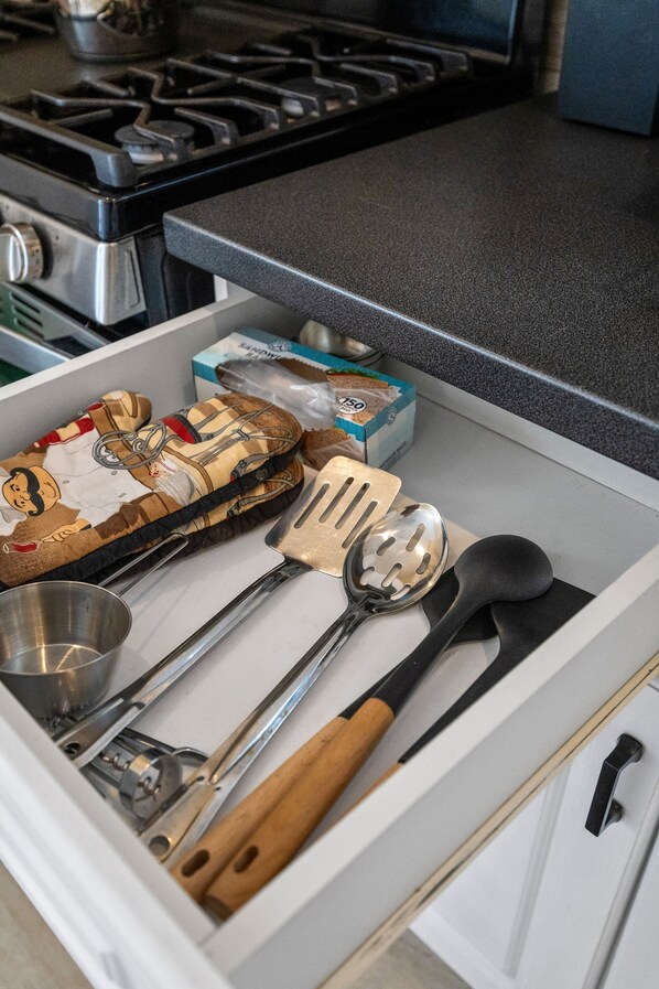 Un cajón de cocina con varios utensilios, una caja de té y una estufa al fondo.