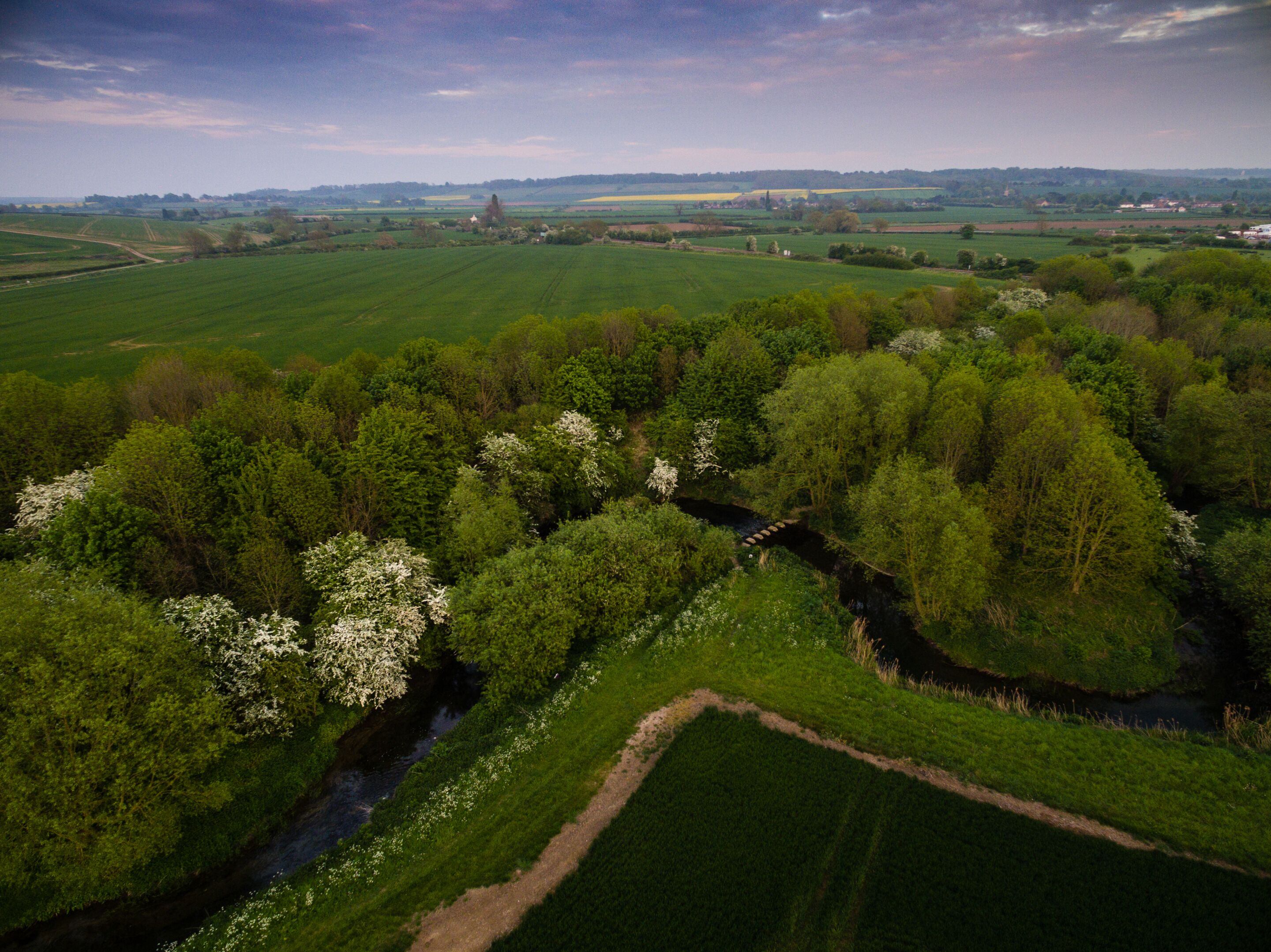 An aerial view of a rural landscape with fields, a river, and a bridge.