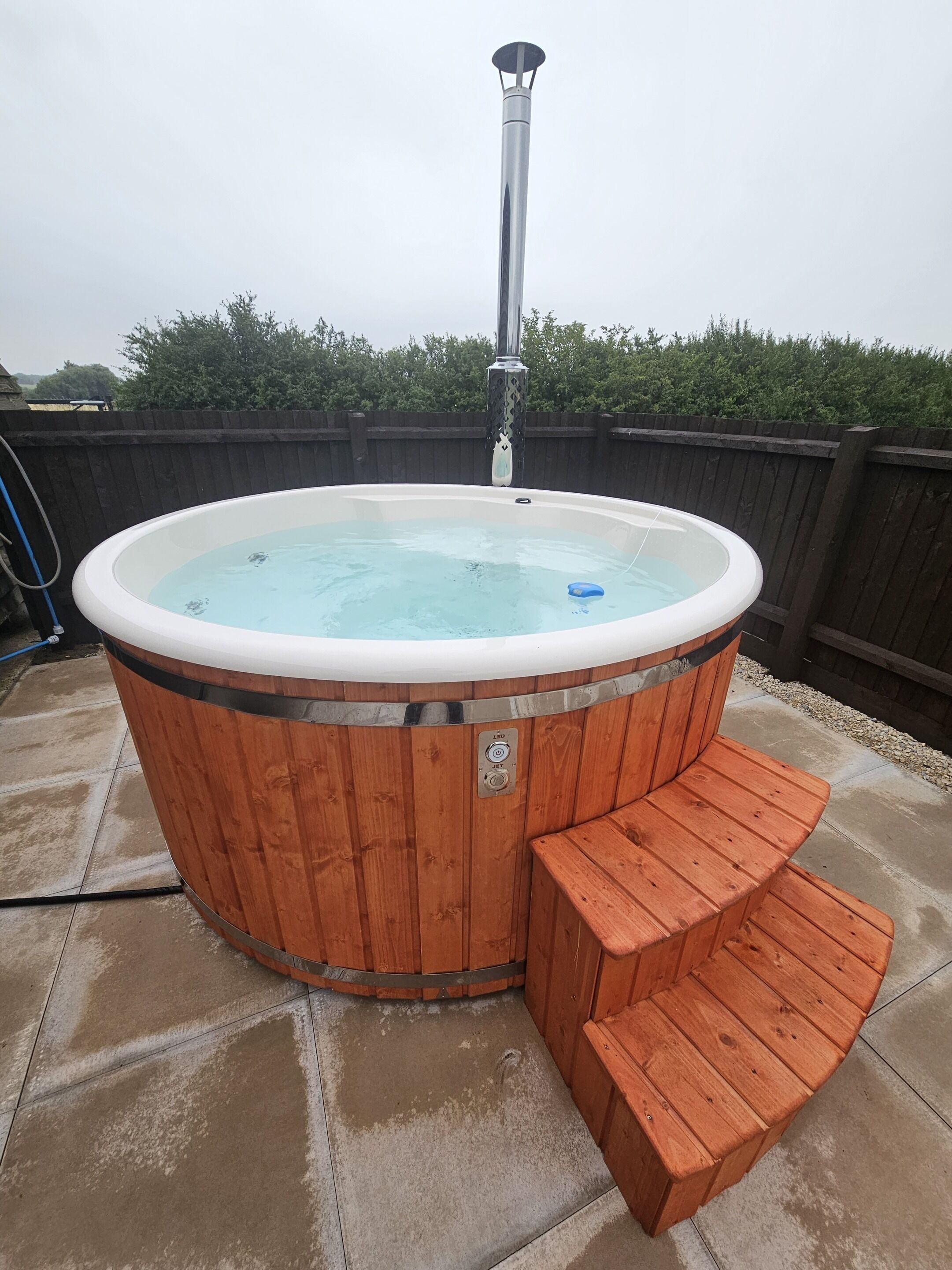 A wooden hot tub with a built-in seat and a control panel, surrounded by a wooden deck.