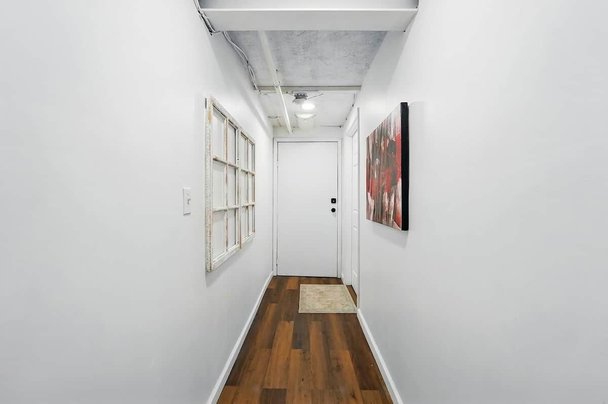 A narrow hallway with wooden flooring, white walls, and a door at the end.
