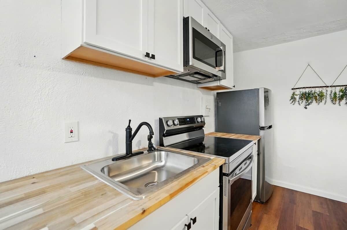 A compact kitchen with white cabinets, a stainless steel sink, a microwave, a stove, and a refrigerator.