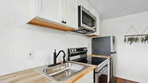 A compact kitchen with white cabinets, a stainless steel sink, a microwave, a stove, and a refrigerator. - Modern Studio W/Parking/Long-Term Ready (Cincinnati)