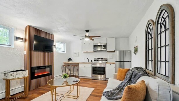 A modern living room with a fireplace, a dining area, and a kitchen with white cabinets and stainless steel appliances. - Modern Studio W/Parking/Long-Term Ready (Cincinnati)