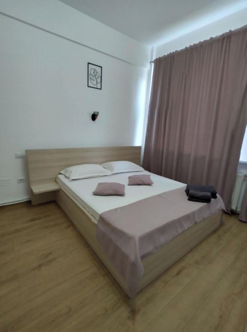 A neatly made bed with pillows and a blanket, a bedside table, and a wall-mounted light fixture.