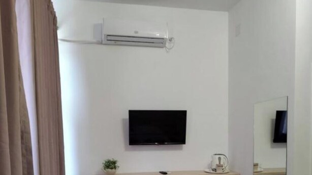 A hotel room with a bed, a desk, a chair, a TV mounted on the wall, a small air conditioning unit, a mirror, and a bedside table with a lamp. - Puzzle Magic (Pitești)
