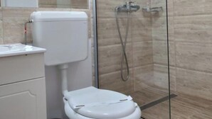 A modern bathroom with a toilet, a glass shower enclosure, and a marble-tiled wall. - Puzzle Magic (Pitești)