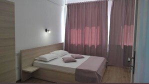 A bedroom with a wooden headboard, a single bed with two pillows, a bedside table, and a window with sheer curtains. - Puzzle Magic (Pitești)