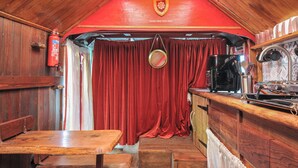 A rustic interior with wooden walls, a red curtain, a wooden table, and a kitchen area with a coffee machine. - Dashing Dennis - 22 (Launceston)