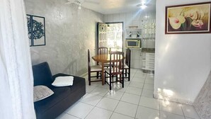 A living room with a dark sofa, a dining table with chairs, and a kitchen area in the background.