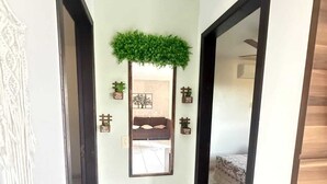 A hallway with a mirror, a green plant, and a bed in the background.