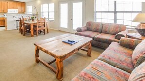 A living room with a wooden coffee table, a patterned sofa, and a dining area with wooden chairs and a table. - 2BR Condo w/ Lake Access & Pool (Lago Vista)