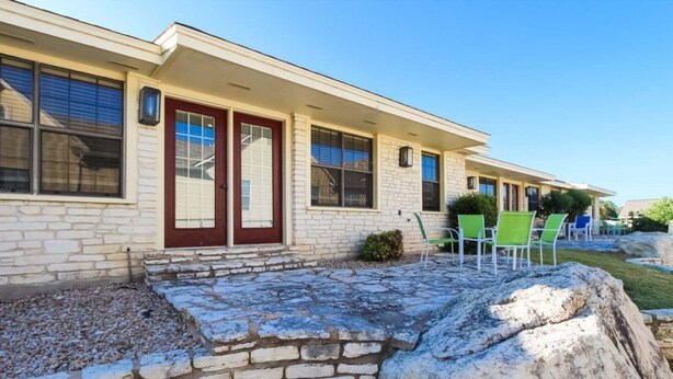 A building with a stone facade, a red door, and a patio area with green chairs. - 2BR Condo w/ Lake Access & Pool (Lago Vista)