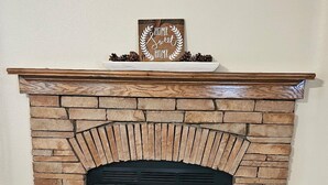 Una chimenea de piedra con un letrero decorativo encima, una cesta de objetos a la izquierda y una olla de metal a la derecha.
