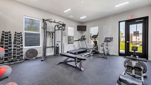 Un gimnasio con máquinas de cardio, equipo de levantamiento de pesas y una banca.
