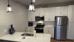 Una cocina moderna con armarios blancos, electrodomésticos de acero inoxidable, una isla grande con pileta e iluminación colgante.