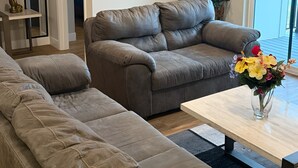 Una sala de estar moderna con un sofá de cuero gris, una mesa de centro con un jarrón de flores y un árbol de Navidad.