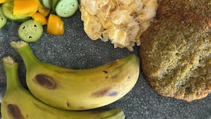 Une assiette contenant des œufs brouillés, des rondelles de concombre, des poivrons, une tranche de banane, une tranche de pain grillé et deux pots de yaourt.