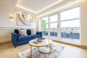 Un salon moderne avec un canapé bleu, une table basse ronde et une grande fenêtre donnant sur un balcon.