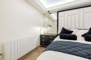 Quarto moderno com uma cama grande, mesa de cabeceira, cômoda, espelho e radiador.