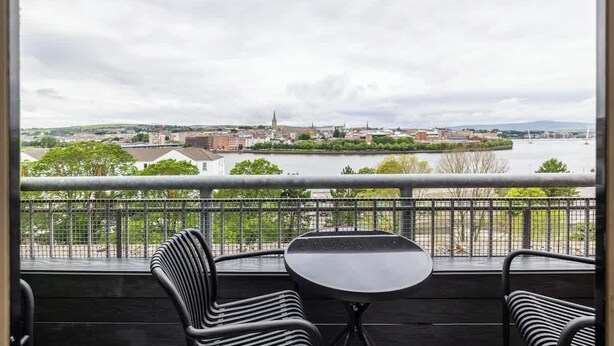 Ein Balkon mit Blick auf eine Stadtansicht, darunter ein Fluss und ein weiter Kirchturm.