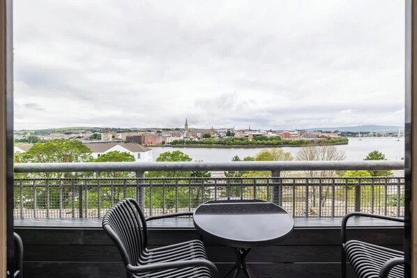 A balcony with a view of a cityscape, including a river and a distant church spire.