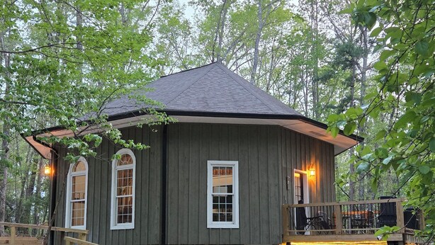 Una cabaña rústica con base de piedra, fachada de madera y un balcón con mobiliario exterior.