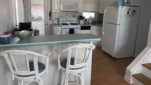 A kitchen with white cabinets, a white refrigerator, a microwave, a stove, and a sink. There are two wicker chairs with blue cushions. - Beach Block 5-Bedroom Retreat with AC in Silver Beach, Lavallette, NJ (Lavallette)
