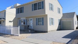 A two-story house with a front porch, a garage, and a white picket fence. - Beach Block 5-Bedroom Retreat with AC in Silver Beach, Lavallette, NJ (Lavallette)