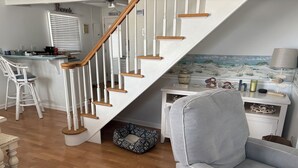 A staircase with wooden steps and white railings, a grey armchair, a white side table with decorative items, and a beach-themed wall mural. - Beach Block 5-Bedroom Retreat with AC in Silver Beach, Lavallette, NJ (Lavallette)