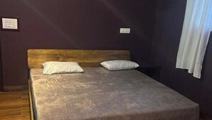 A single bed with a wooden headboard in a room with dark walls and a wooden floor. - Coorg Tree House Tent (Madikeri)